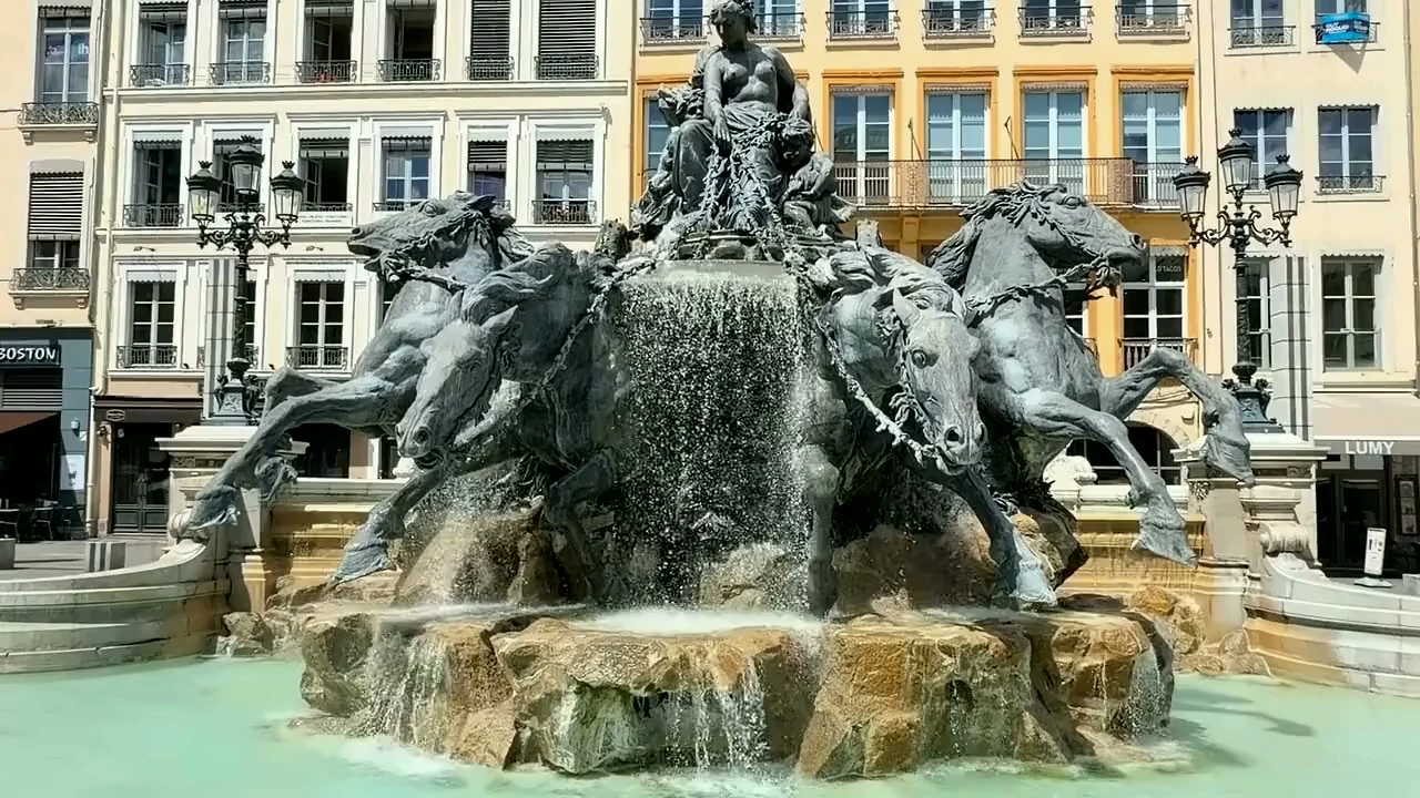 La fontaine Bartholdi, place des Terreaux à Lyon : une figure féminine sur un char tiré par quatre chevaux, l’eau sur les rochers et les façades de la place